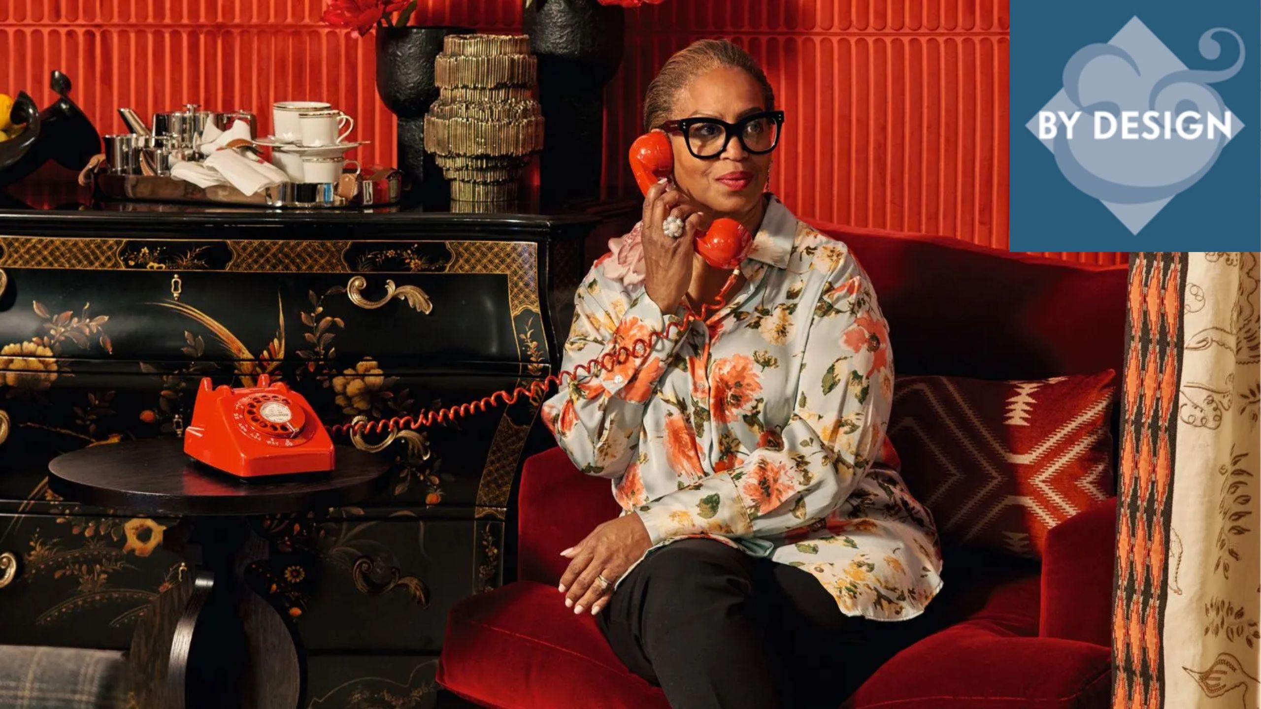 Joy Moyler sat in a red armchair in a red room, holding a red telephone to her ear. Antique dresser decorated with ornaments to her left