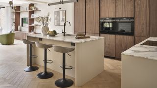 kitchen with floor to ceiling wooden cabinets, kitchen island with marbled top, breakfast bar stools and herringbone wooden floor