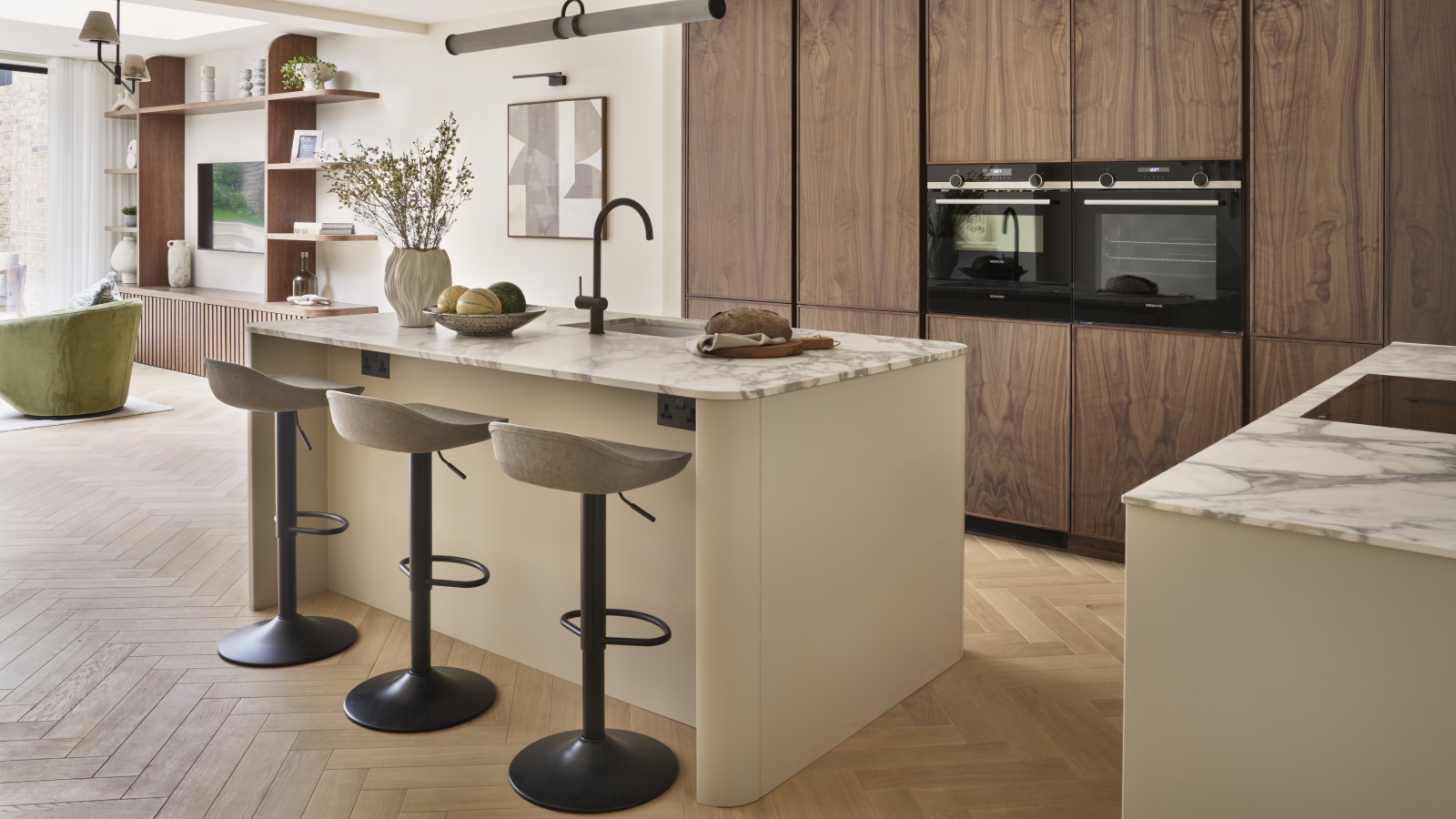 kitchen with floor to ceiling wooden cabinets, kitchen island with marbled top, breakfast bar stools and herringbone wooden floor