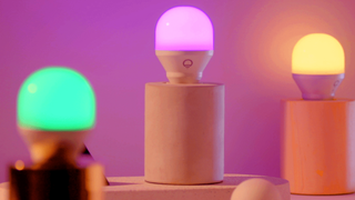 Tre stycken LIFX Mini Color står på varsin vit pelare och lyser i grönt, rosa och gult.