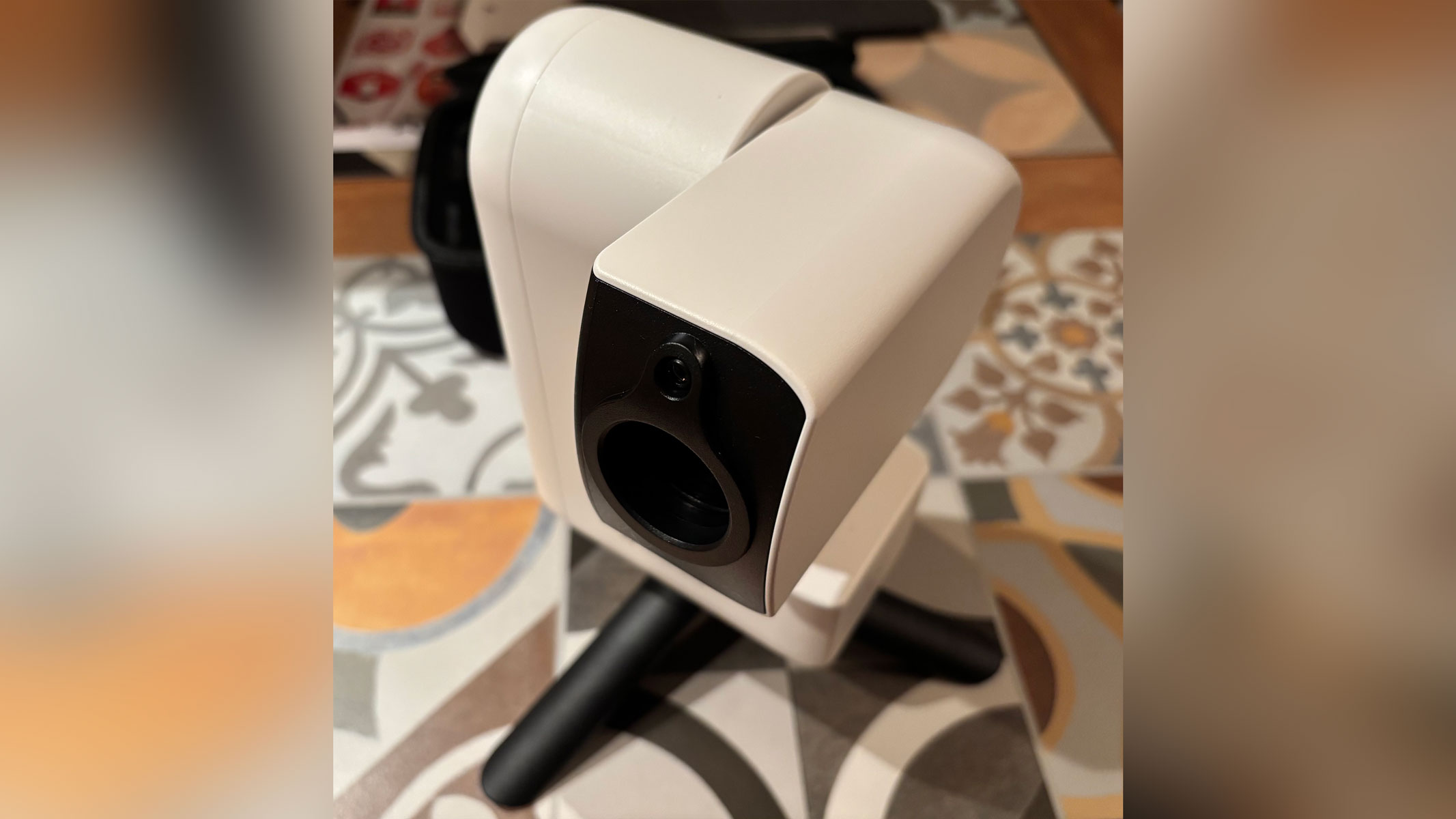 A white smart telescope with a black lens is standing on black legs on a tiled surface.