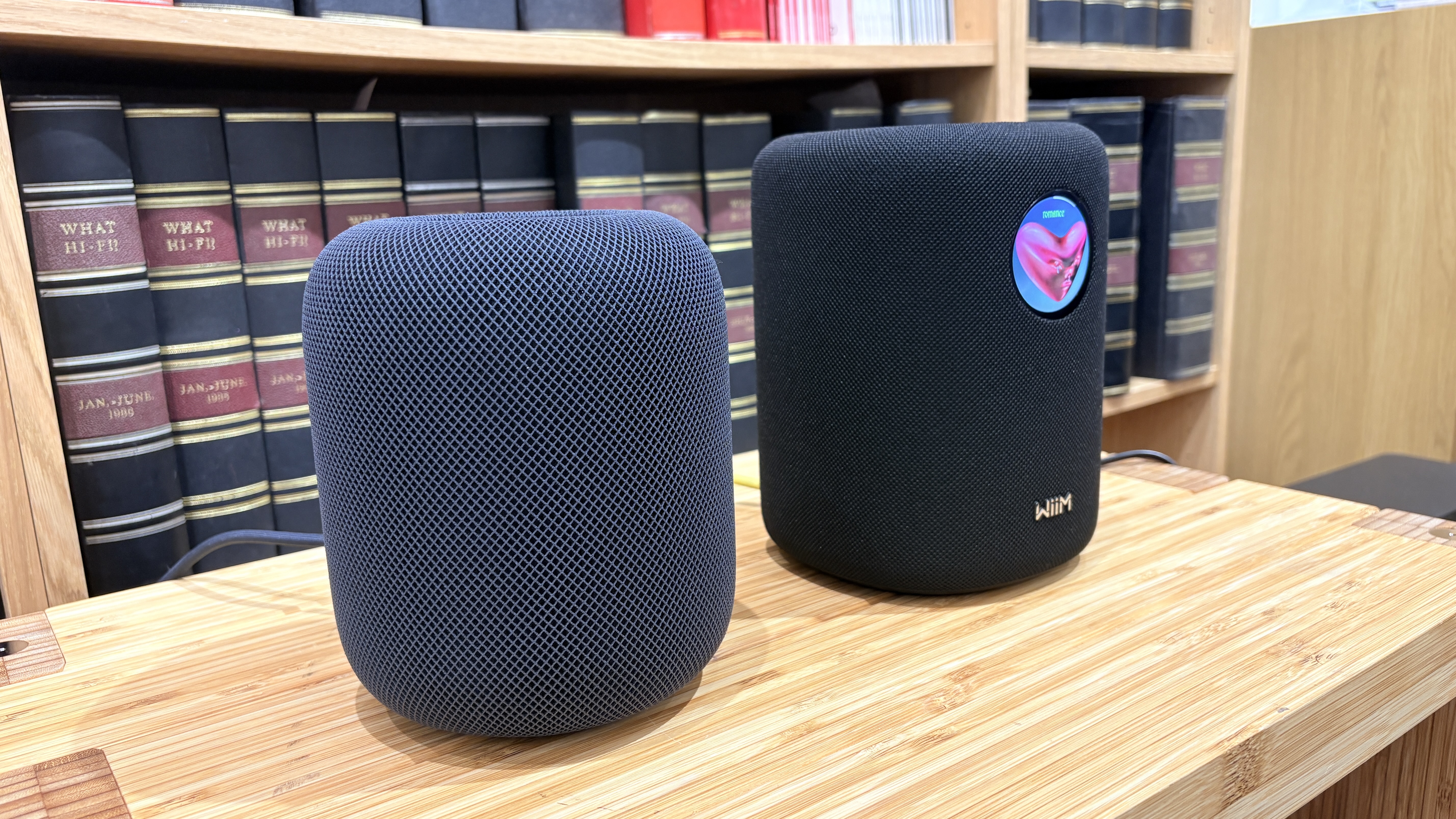 A black Apple HomePod 2 next to a black WiiM sound on a wooden surface