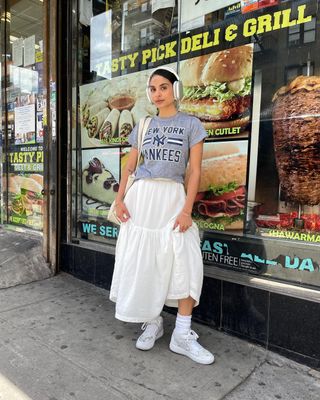 @danie.sierra posing while wearing Yankees T-shirt, white maxi skirt, and white sneakers