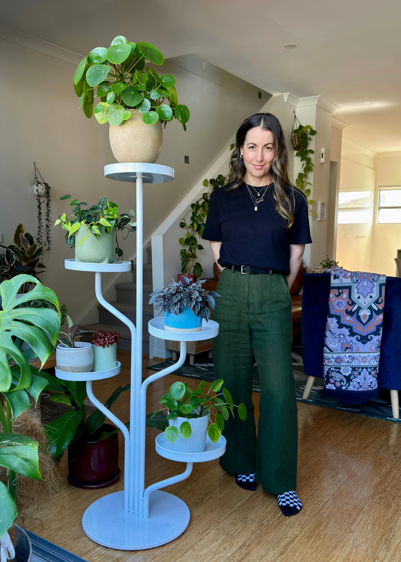 Jacintha Webster standing beside a plant pedestal decorated with her collection of potted houseplants