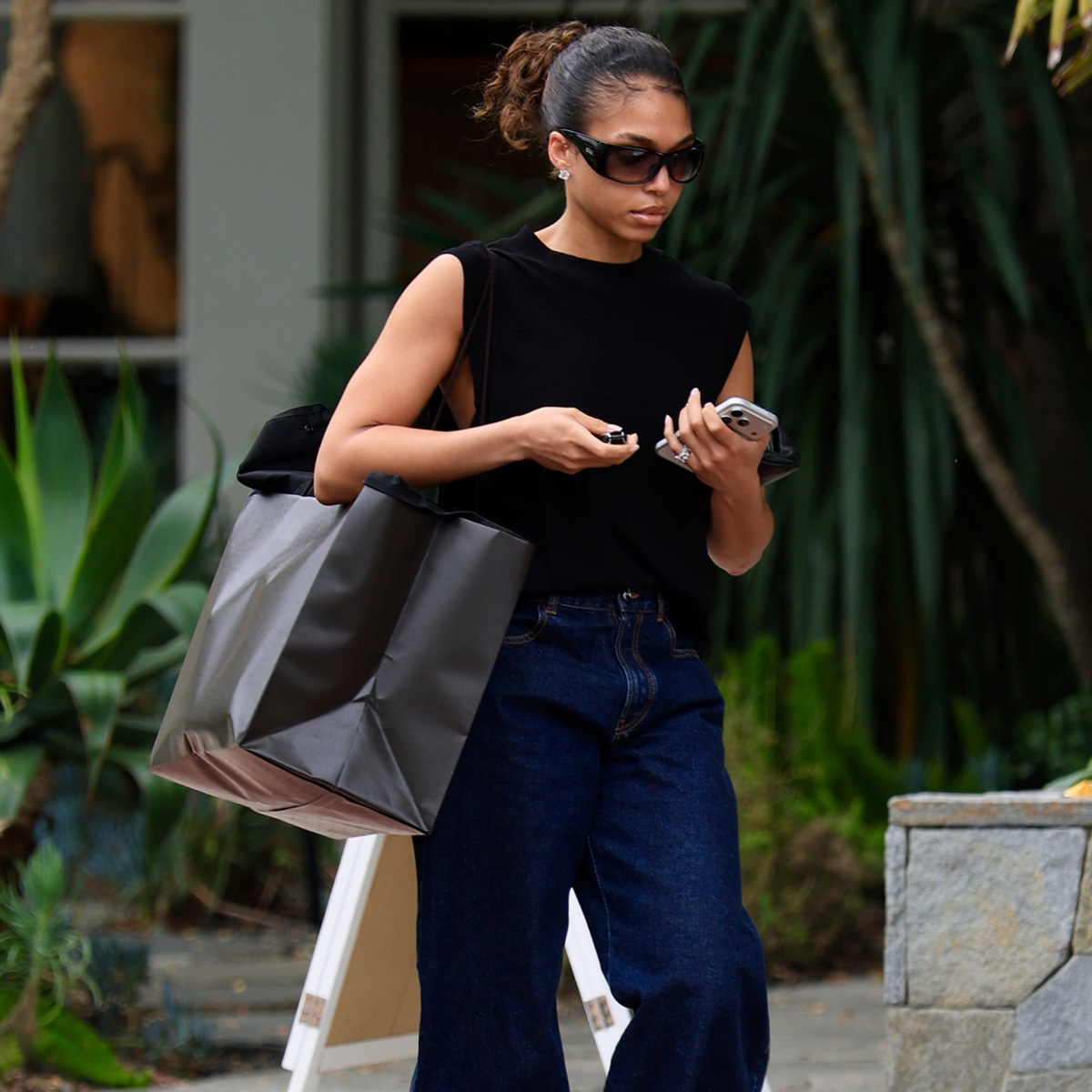 Lori harvey wears a black tank top with dark-wash jeans and sunglasses.