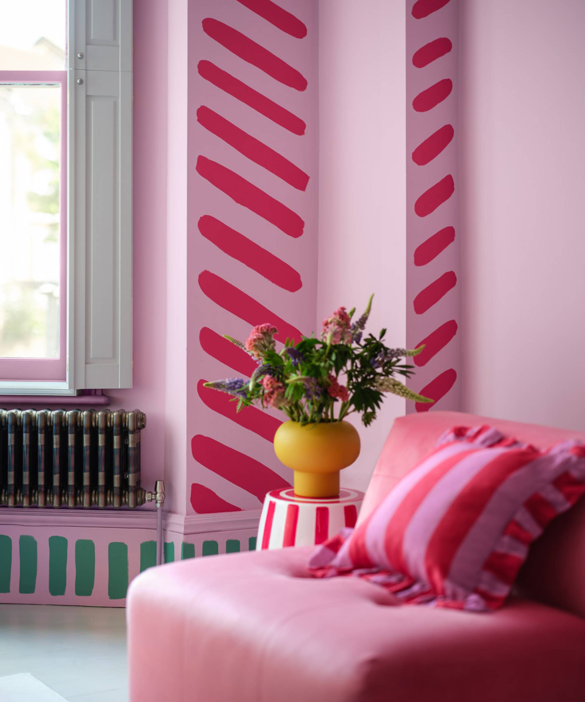 living room with pink walls, with small wall returns painted with bright pink diagonal stripes and green vertical stripes on skirting board