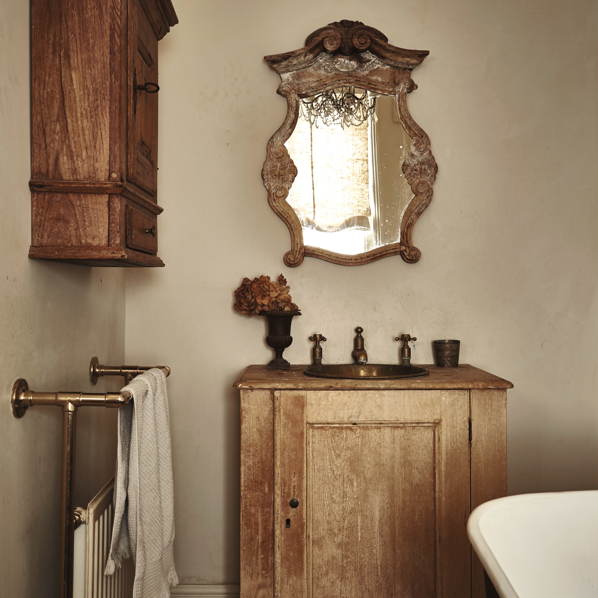 bathroom with plaster coloured walls, antique mirror, wooden vanity unit with inset antique brass basin, and towel rail