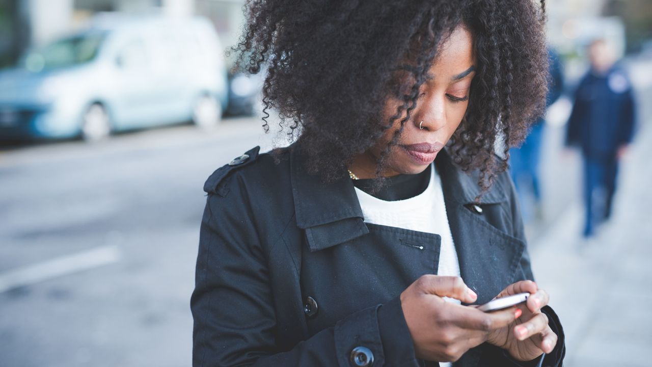 Woman in black trench coat texting