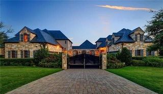 The exterior of a mansion with a large drive and a green front lawn