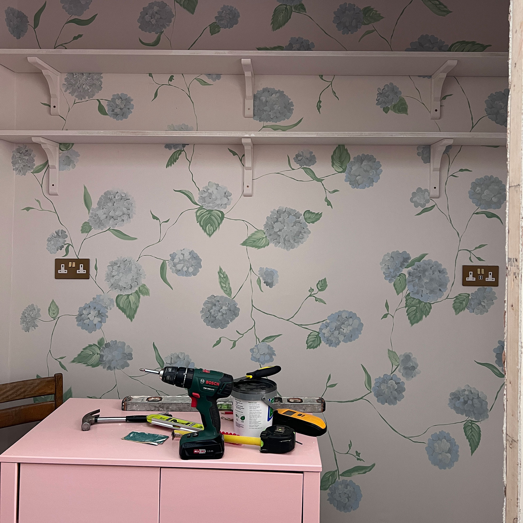 Power and DIY tools sitting on pink cabinet in room with blue hydrangea wall motif