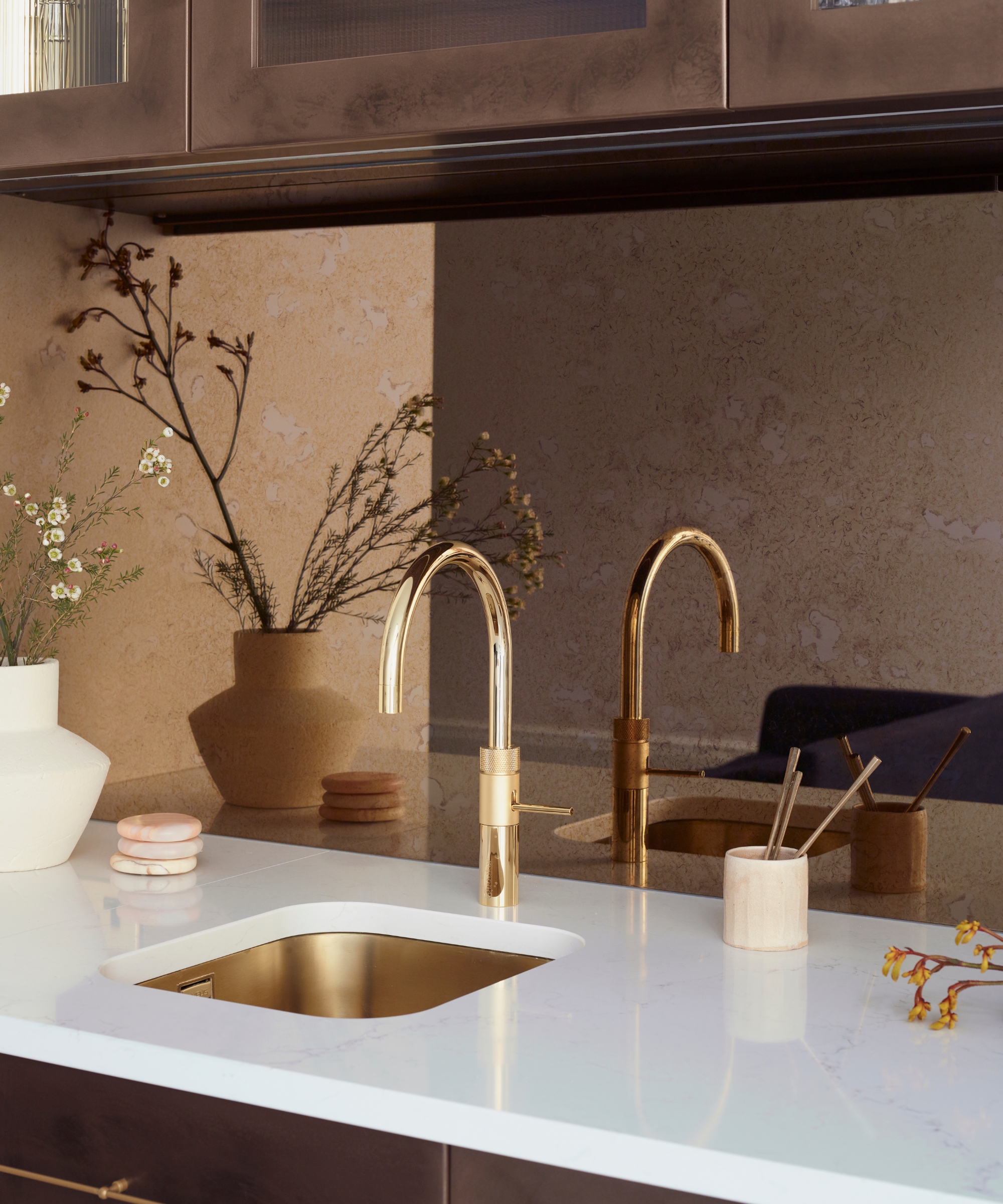 A antique mirror finish backsplash behind a gold sink and white countertop