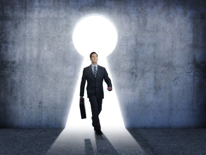 Investor carrying a briefcase walking through an illuminated keyhole