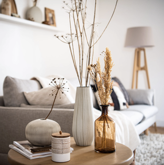 Maison du Monde dried flowers, vases on a side table next to grey couch.