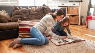 Mother sat on the floor with young girl looking at one of the best photo albums