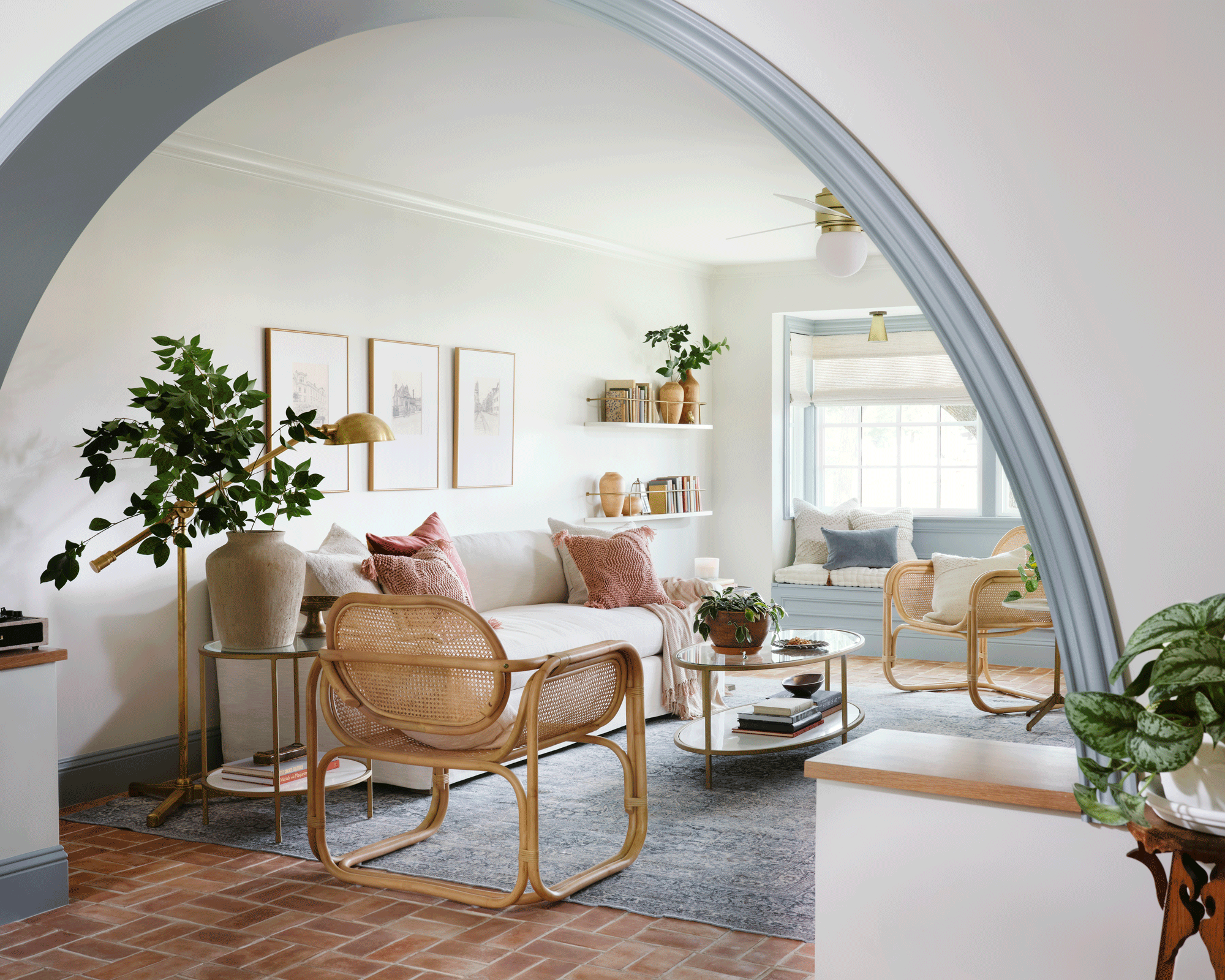 archway in a Texas home, with white furniture, wicker chairs, a tile floor and a blue rug, and soft white paintings on the wall, with white floating shelves