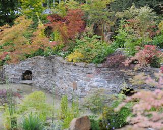 An example of Japanese garden ideas showing a stone wall surrounded by trees