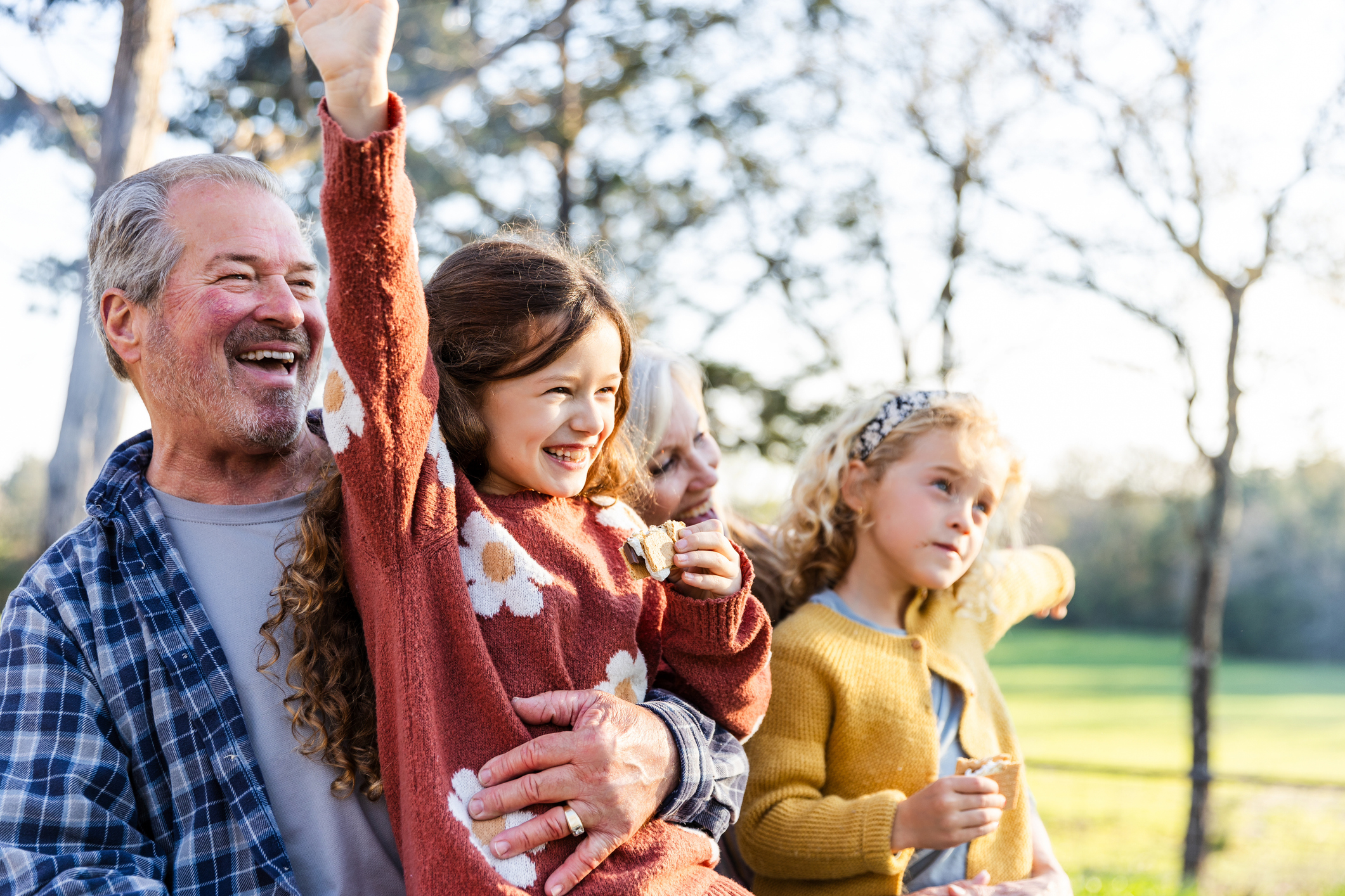 While enjoying the fall weather and eating smores, the two senior adult grandparents and their two elementary age granddaughters act silly for a photo.