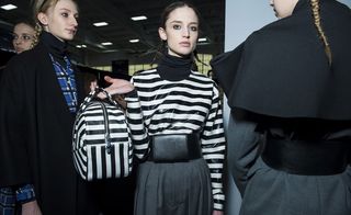 Girl in black and white top poses for a picture holding a striped black and white bag in between people