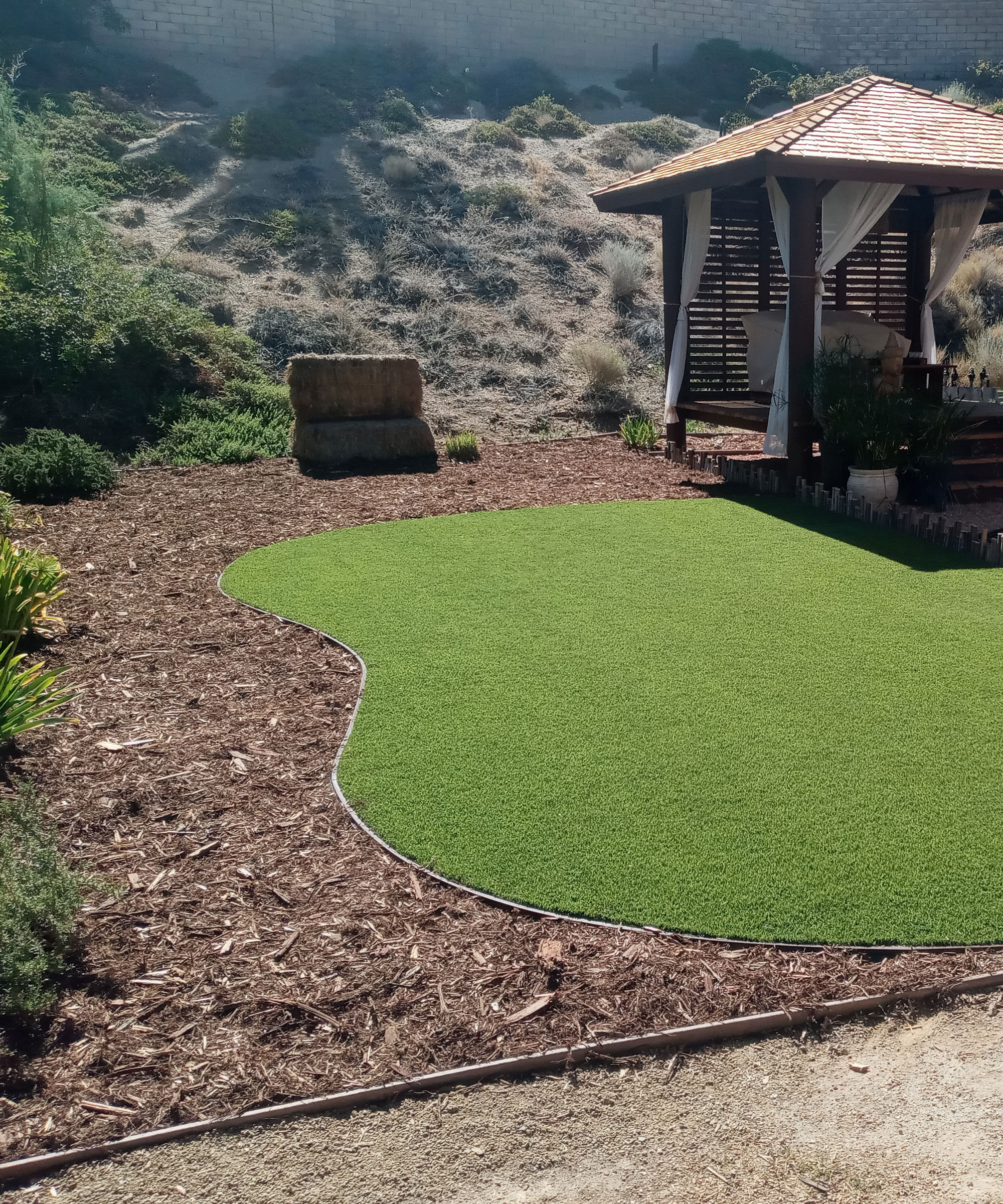 area of lawn with path made of natural materials edged with bender board, with a gazebo with drapes and planting