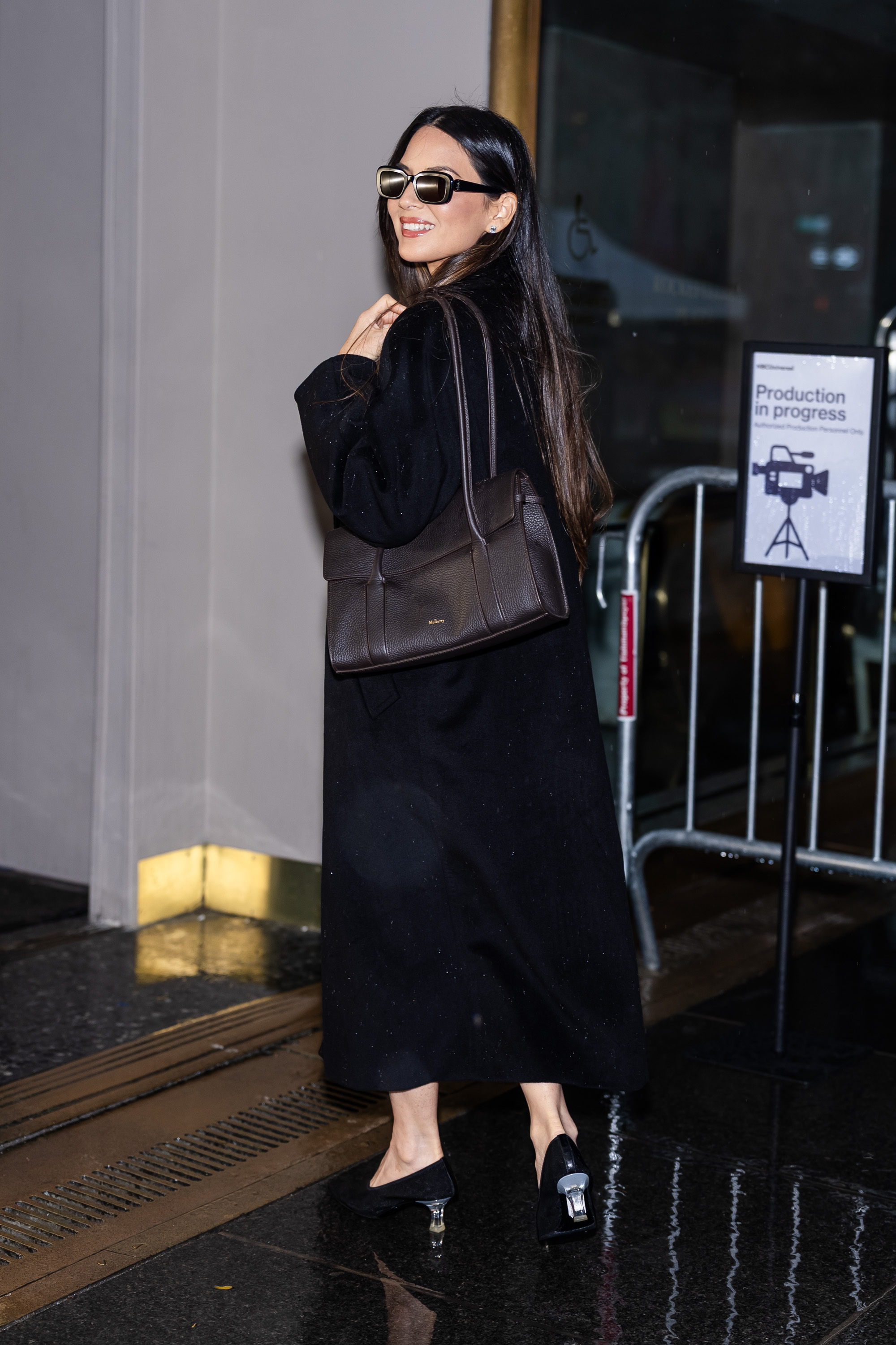 Olivia Munn wearing a black coat, brown bag, and black heels.