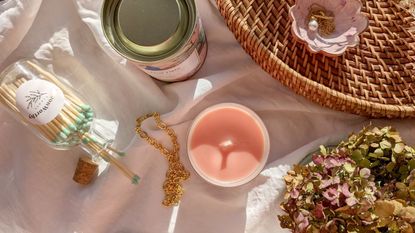 top down image of a pink, unburnt candle beside a jar of matches on its side, a can, a woven tray, and some dried hydrangea flowers. 