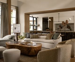 Neutral living room with cream sofa, brown armchairs and stone coffee table, wooden beams onlooking to the kitchen