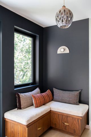 Matt black painted hallway with wooden seating ceramic lighting fitting and earthy toned cushions