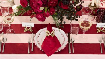 Red and white themed christmas table with striped table cloth, bow napkins and place holders, red flower centerpiece and wine glasses 