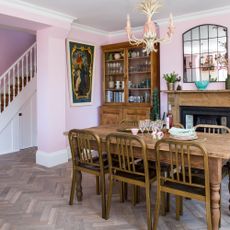 Dining area of basement kitchen with chevron floor, pink walls, wooden dining table and sideboard