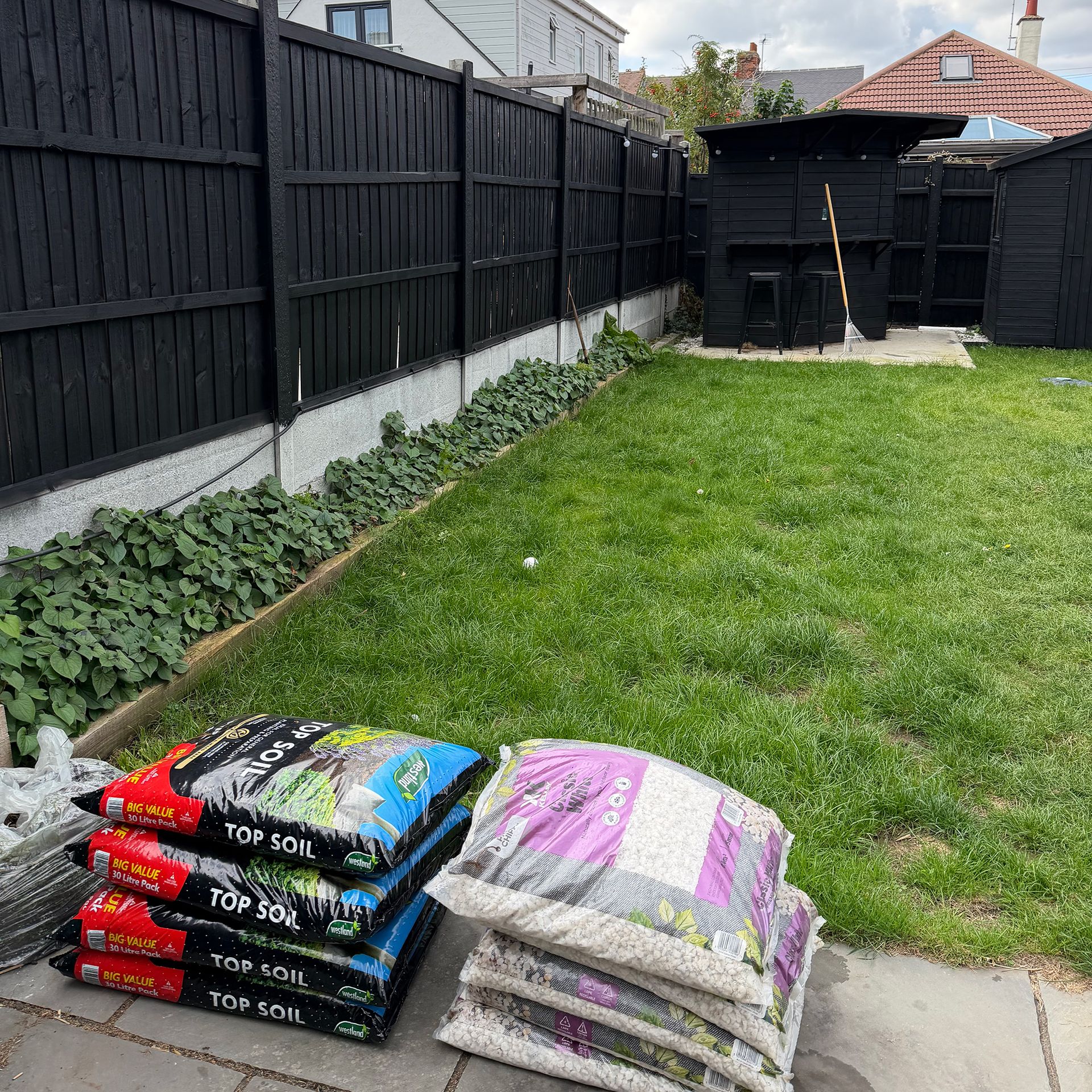 Piles of bags full of soil and stone on patio in front of lawn area