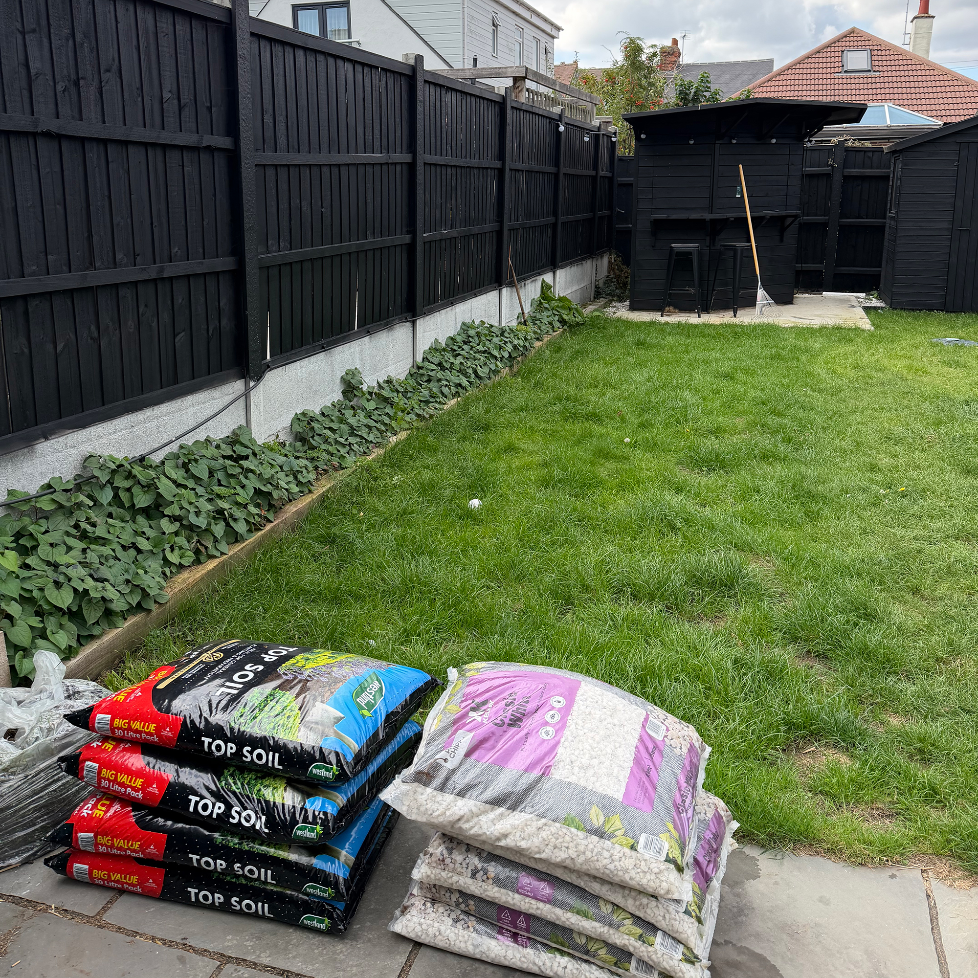 Piles of bags full of soil and stone on patio in front of lawn area