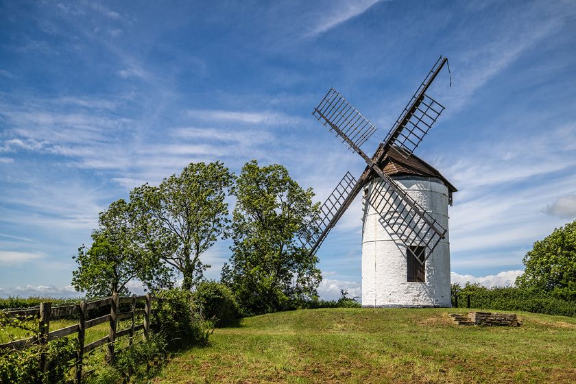 white windmill on mound of green with blue sky background
