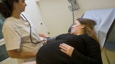 a nurse adjust a blood pressure cuff on a pregnant woman's arm as the patient lays down on a covered hospital table