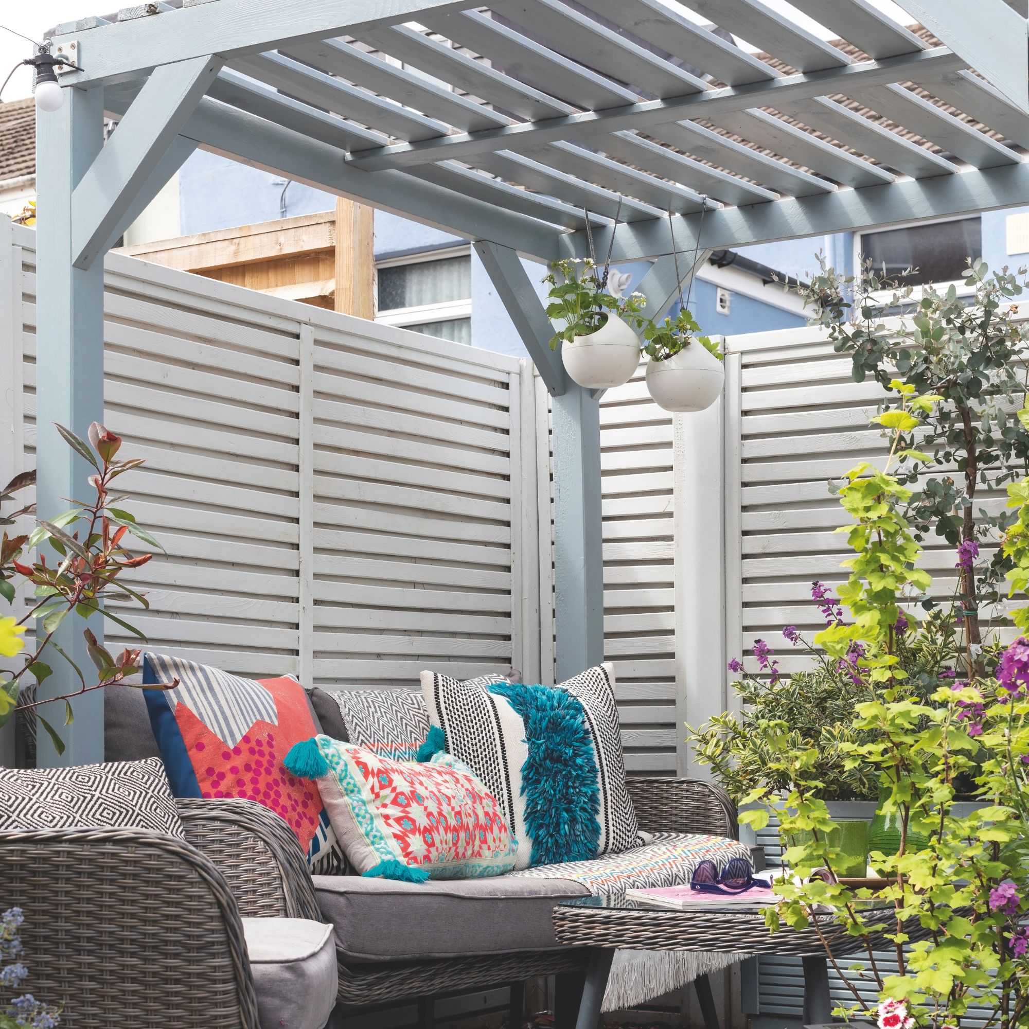 Light blue painted wooden pergola covering rattan garden furniture set with patterned cushions