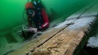 A diver with a notepad looks at a wooden. boat underwater