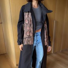 Influencer wearing a black trench,tee, jeans, and a fringed paisley scarf