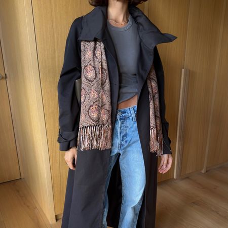 Influencer wearing a black trench,tee, jeans, and a fringed paisley scarf