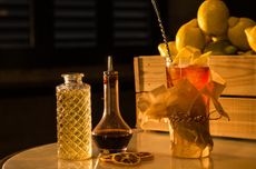 A cocktail on a table with jars and a box of lemons