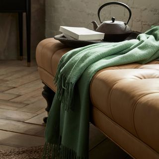 A green Williams Sonoma European Solid Cashmere Throw draped over a bench