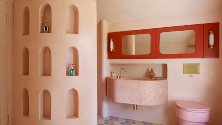 A small bathroom painted an earthy pink, with red cabinets and a candy-toned WC