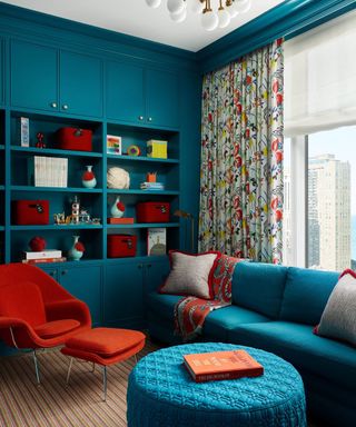 teal living room with bright orange and red chair and accessories, stripe rug, bright drapes, teal couch and footstool