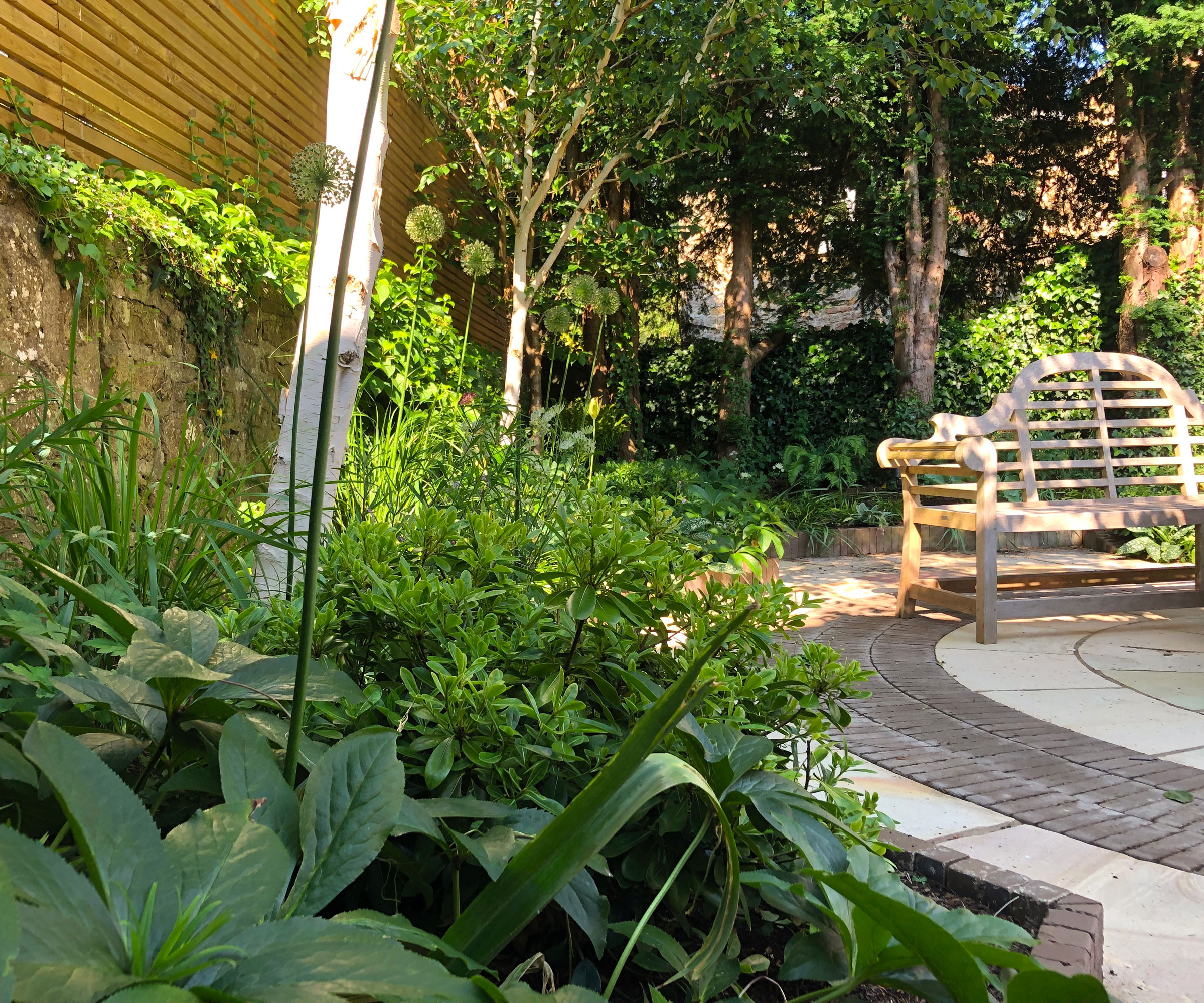 circular patio with garden bench surrounded by trees and shrubs