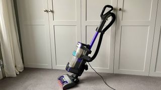 The Shark Anti Hair Wrap Upright Vacuum Cleaner with Powered Lift-Away NZ850UK leant against a set of cupboards