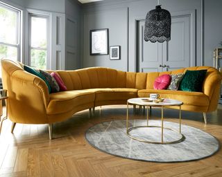 Shapely, curved sofa in Turmeric hued velvet upholstery, contrasted against mid-tone gray walls and painted doors.