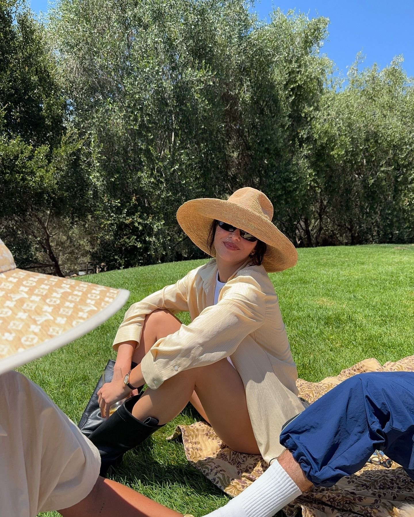 Kendall Jenner wears a straw hat, yellow shirt, and black pull-on boots.
