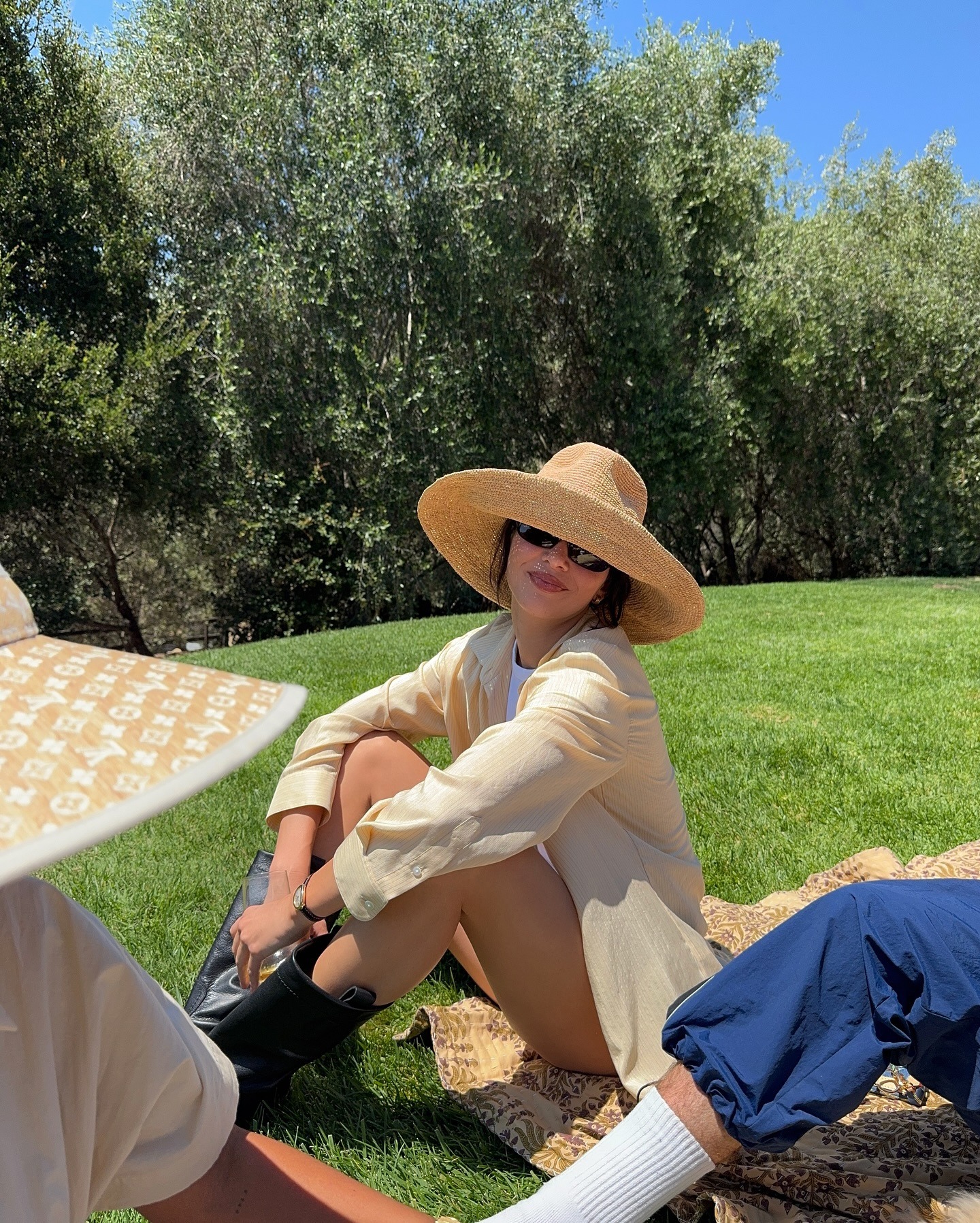 Kendall Jenner wears a straw hat, yellow shirt, and black pull-on boots.