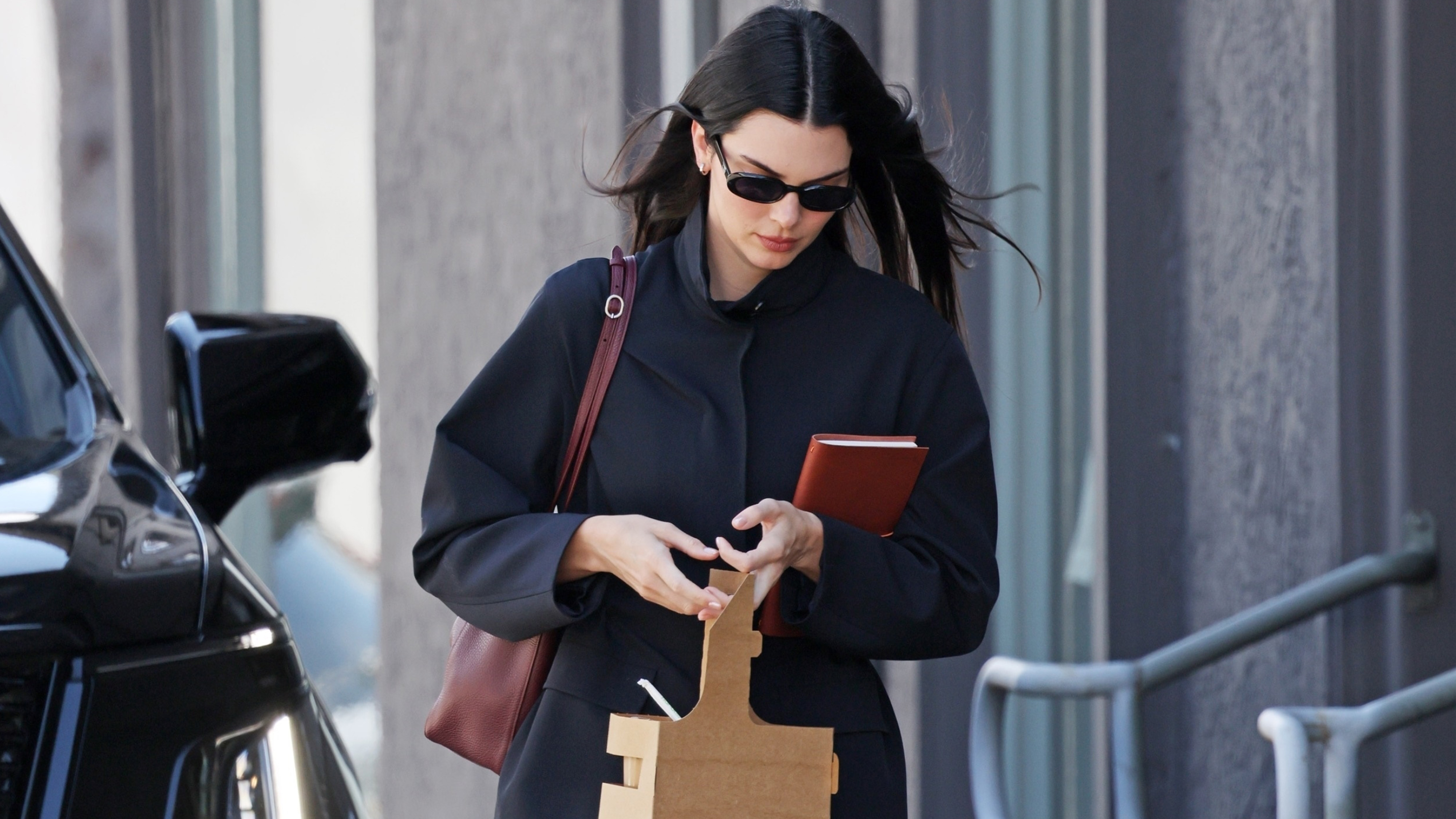 Kendall jenner wears a navy jacket with a burgundy bag.