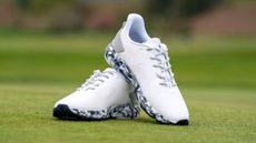 The stunning G/FORE MG4+ Shoe in its white and grey colorway resting on the green