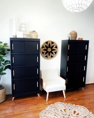Two freshly painted black bookcases with wooden hardware staged in living room with hardwood floors and white walls