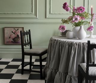 A dining room with a checkerboard flooring and ticking stripe upholstered chairs and tablecloth